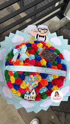 a large cake decorated with multicolored roses on top of a wooden table next to a person's feet