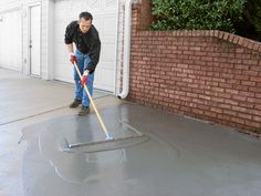 a man with a mop is cleaning the cement on his driveway while holding a broom