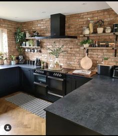 a kitchen with brick walls and black cabinets, an oven, counter tops, and potted plants on shelves