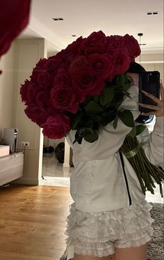 a woman taking a selfie with her cell phone and bouquet of roses in front of her face