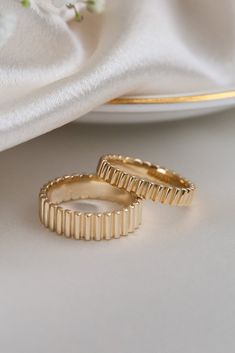 two gold wedding rings sitting on top of a white cloth next to a plate with flowers