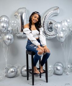 a woman sitting on top of a stool in front of balloons and the number six