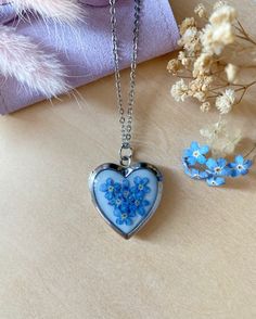 a blue heart shaped necklace sitting on top of a table next to a vase with flowers