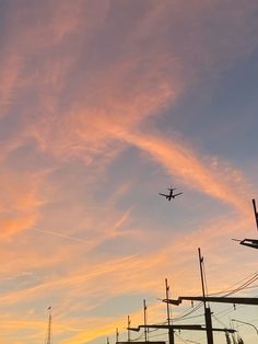 an airplane is flying high in the sky at sunset or dawn, with power lines and telephone poles behind it