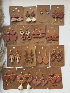 many different types of earrings are displayed on brown tags with white tassels and gold earring hooks