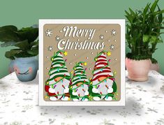 a christmas card with three gnomes on it next to plants and potted plant