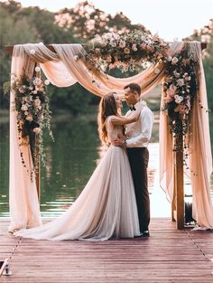 a bride and groom are kissing on the dock at their wedding ceremony in front of water