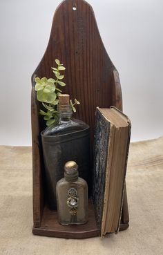 an old book, vase and flask on a wooden chair with a plant in it