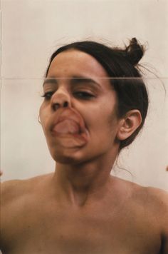 a woman sticking her tongue out in front of a mirror with the reflection of another person's face