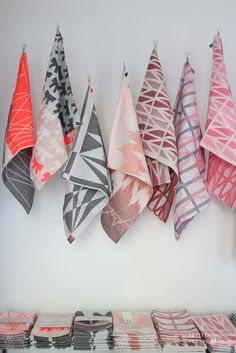 towels hanging from hooks on the wall in front of a white wall with several different designs