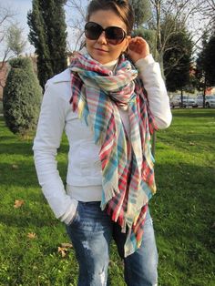 a woman standing in the grass wearing sunglasses and a plaid scarf