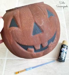 a pumpkin shaped pot sitting on top of a tile floor next to a paintbrush