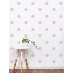 a white table with a potted plant sitting on top of it next to a pink polka dot wallpaper