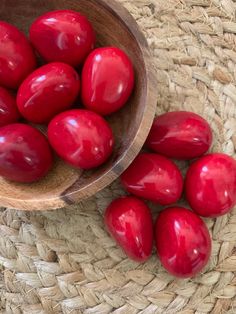 a wooden bowl filled with red eggs on top of a woven mat