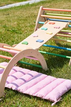 two children's play equipment in the grass with pink and green cushions on them