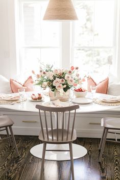 a dining room table with flowers in the center and place settings on the chairs around it