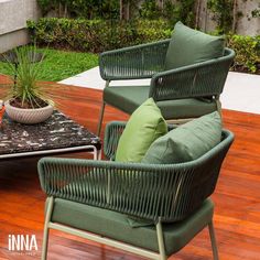 two green chairs sitting on top of a wooden floor next to a table and potted plant