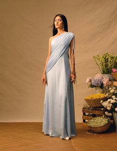 Elevate your style with our Powder Blue Ruching Saree Dress, a harmonious fusion of modern and ethnic charm. The traditional saree drape-like pallu adds an authentic touch, while the fitted upper body seamlessly transitions into a flared dress. The finely ruched panel across the body makes it ideal for any fusion outfit inspiration. Embrace sophistication and versatility with this exquisite dress, perfect for making a memorable statement at any occasion.Product details: Material - Modal Satin, V Draped Shoulder Dress, Modern Indian Dress, Exec Photoshoot, Western Gowns, Saree Drape, Mob Dress, Blue Drapes, Tulle Midi Dress, Drape Dress