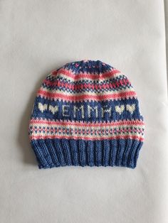 a blue and red knitted hat sitting on top of a white sheet with the word mmm written in it