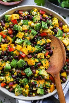 a bowl filled with black beans, corn and avocado salad next to a wooden spoon