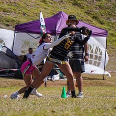 two girls are playing frisbee on the grass in front of tents and people