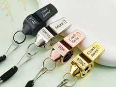 four different colored metal whistles on a white table next to a computer mouse and keyboard