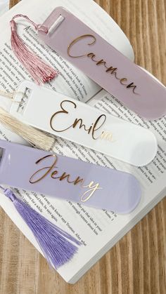 three personalized bookmarks sitting on top of an open book with tassels