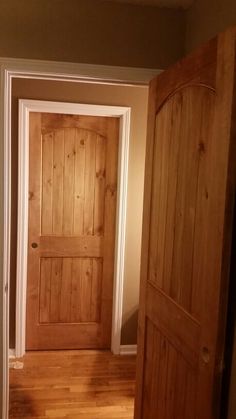 an empty room with two wooden doors and hard wood flooring on the other side