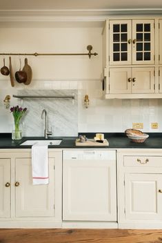 a kitchen with white cabinets and black counter tops, wooden flooring and hanging utensils