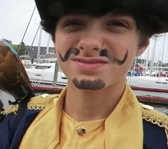 a young man with fake mustaches on his face in front of a boat dock