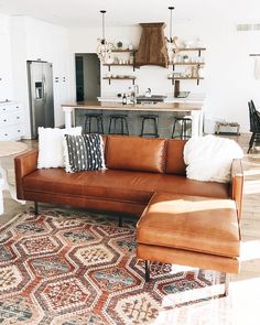 a living room filled with furniture and lots of pillows on top of a rug in front of a kitchen