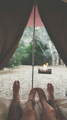 two people are laying in bed under an umbrella with the view of a campfire