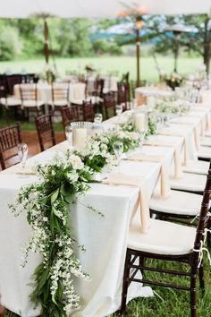 a long table with white flowers and greenery is set up for an outdoor wedding