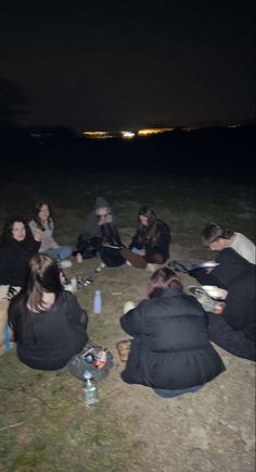 a group of people sitting on top of a grass covered field next to each other