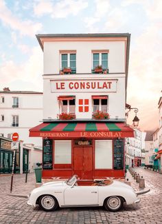 an old car is parked in front of a small restaurant on a cobblestone street