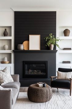 a living room with black walls and white carpeted flooring, a gray couch, two chairs, a coffee table and a fireplace in the center