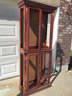 a tall wooden display case sitting in front of a garage door on the side of a house