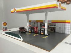 a toy gas station with cars parked at the pump and signs on the wall above it