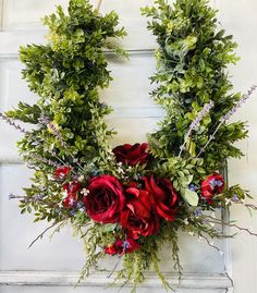 a wreath with red flowers and greenery hanging on a door