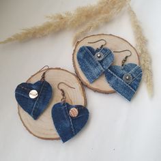 two pieces of denim heart shaped earrings on wooden slices with feathers in the back ground