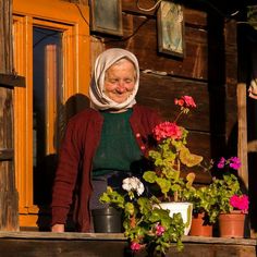 an old woman is standing on the porch with potted flowers in front of her