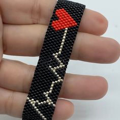 a hand holding a black beaded bracelet with a red heart on it