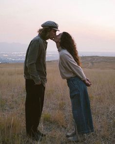 a man and woman standing in a field kissing each other while the sun is setting