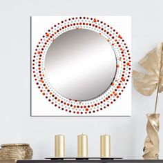 a round mirror hanging on the wall above a table with candles and vases in front of it