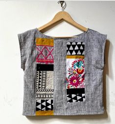 a gray top with colorful patchwork on the front and back, hanging from a wooden hanger