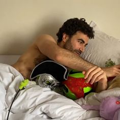 a shirtless man laying in bed next to a stuffed animal and flower pot on the pillow