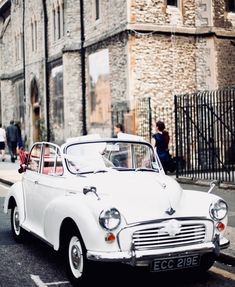 an old white car is parked on the side of the road in front of a building