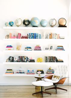 a white book shelf filled with lots of books next to a chair and table on top of a hard wood floor