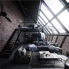 a living room filled with lots of furniture next to a loft type building wall covered in windows