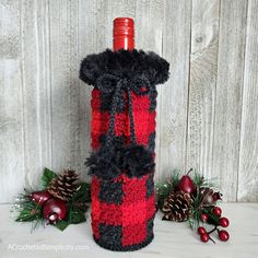 a red and black plaid wine bottle cozyie next to pine cones, berries and evergreens